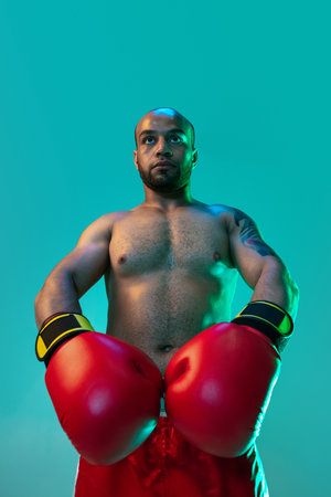 Bottom view. One professional boxer standing with hands down over blue green background in neon...