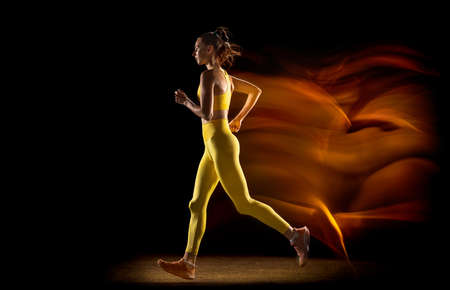 Young woman, female athlete training isolated over black studio background in mixed neon lights....