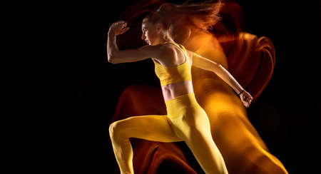Side view. Portrait of young female athlete in motion isolated over black studio background in mixed neon lights.の写真素材