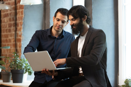 Young men working in modern office using devices and gadgets. Making reports, analitycs, routine processing tasksの写真素材