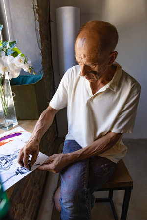 Mature or senior painter or artist with graphite crayon in front of camera. Man in a paint-stained shirt working at studioの写真素材