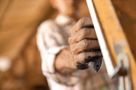 Mature or senior grey painter with a brush standing in front of camera. man in a paint-stained shirt working at studio or homeの写真素材