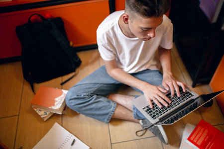 One young caucasian guy, student sitting at floor with laptop over home or library background.の写真素材