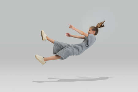Studio shot of little preschool caucasian girl in casual clothes falling down isolated over white...
