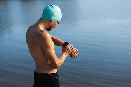 Professional triathlete before swimming in rivers open water. Man wearing swim equipment practicing triathlon on the beach in summers day.の写真素材