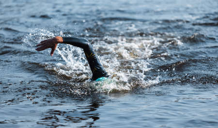 Professional triathlete swimming in rivers open water. Man wearing swim equipment practicing triathlon on the beach in summers day.の写真素材