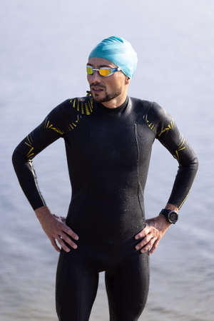 Professional triathlete before swimming in rivers open water. Man wearing swim equipment practicing triathlon on the beach in summers day.の写真素材