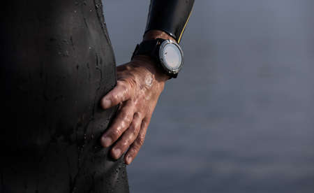 Professional triathlete before swimming in rivers open water. Man wearing swim equipment practicing triathlon on the beach in summers day.の写真素材
