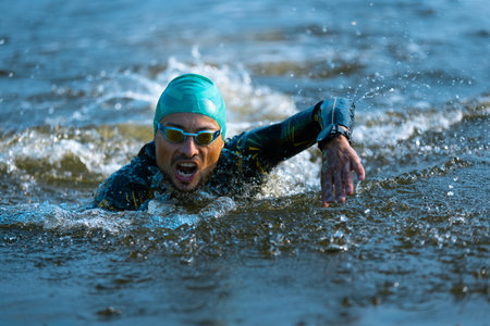 Professional triathlete swimming in rivers open water. Man wearing swim equipment practicing triathlon on the beach in summers day.の写真素材