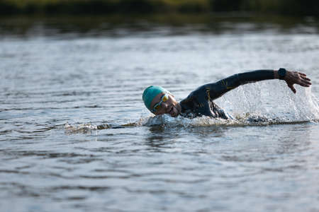 Professional triathlete swimming in rivers open water. Man wearing swim equipment practicing triathlon on the beach in summers day.の写真素材