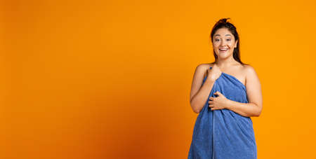 Adorable beautiful plump woman with big bath towel isolated over orange studio background.