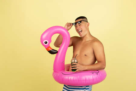 One young smiling handsome asian man in trunks with swimming circle isolated over yellow studio background.の写真素材