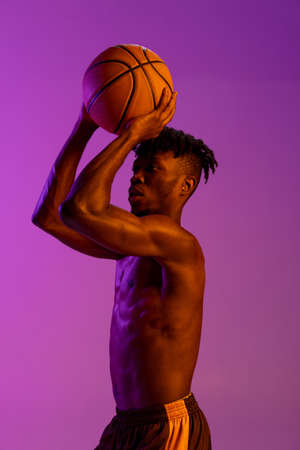 Young african man, basketball player practicing with ball isolated over purple neon background.