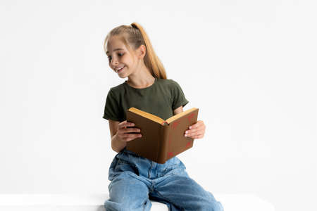 Smiling. One teen cute caucasian girl in casual clothes reading book, looking away isolated over white studio background. Copyspace for ad.の写真素材