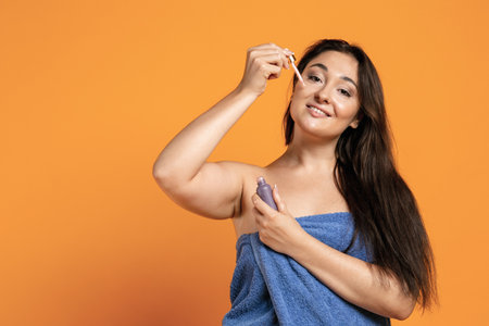 Adorable beautiful plump woman with big bath towel isolated over orange studio background.の写真素材