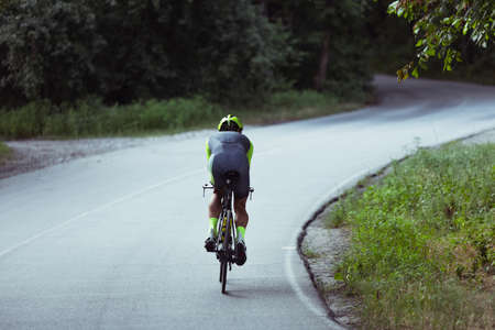 Young male triathlete riding a bicycle on the open road. Professional sportsman is engaged in triathlon on bright summer dayの写真素材