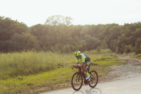 Young male triathlete riding a bicycle on the open road. Professional sportsman is engaged in triathlon on bright summer dayの写真素材