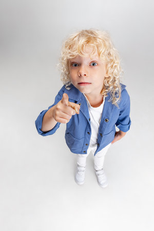 Cute little curly preschool boy in casual clothes looking at camera isolated over white studio background.の写真素材