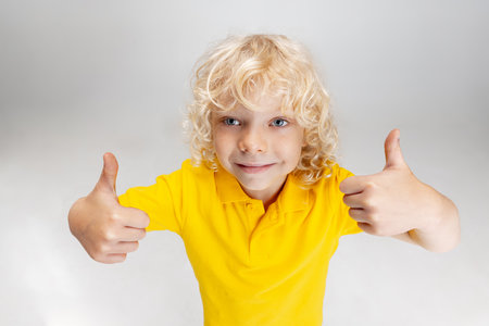 Cute little curly preschool boy having fun, playing isolated over light studio background.の写真素材
