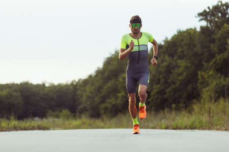 Young professional male triathlete, runner in motion on open road. Concept of sport, lifestyle,...