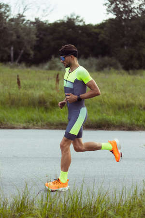 Young professional male triathlete, runner in motion on open road. Concept of sport, lifestyle,...