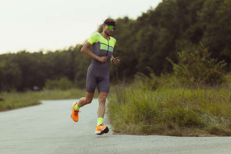 Image of young professional male triathlete, runner in motion on open road. Concept of sport,...