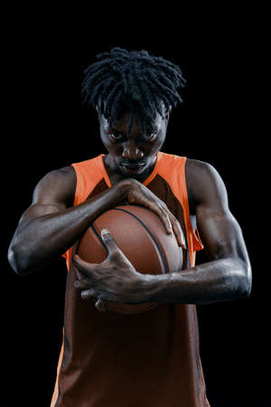 Close-up. Professional african basketball player posing with ball isolated over dark studio background.の写真素材