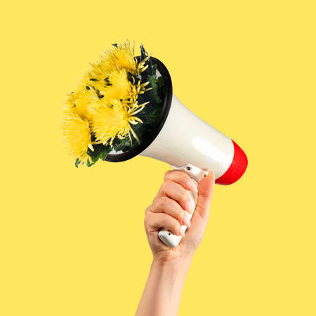 Contemporary art collage. Human hand holding loudspeaker with sticking out flowers on yellow background.の写真素材