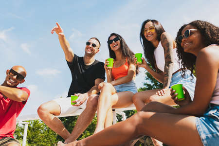 Group of young people, men and women resting on the beach, drinking cool drinks, having fun, sunbathingの写真素材