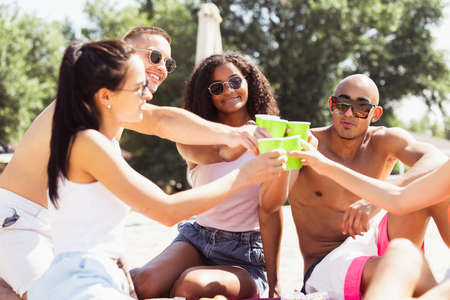 Group of young people, men and women resting on the beach, drinking cool drinks, having fun sunbathingの写真素材