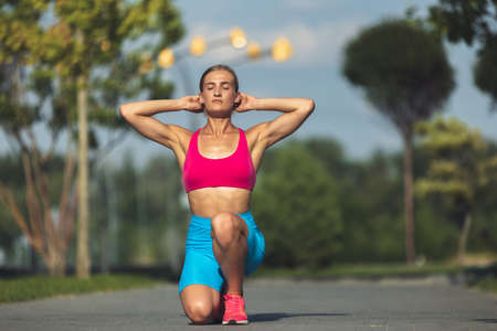 Young slim sportive caucasian woman working out, doing fitness, yoga in the park or on city street.
