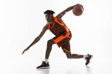 Young african man, professional basketball player training with ball isolated over white studio...