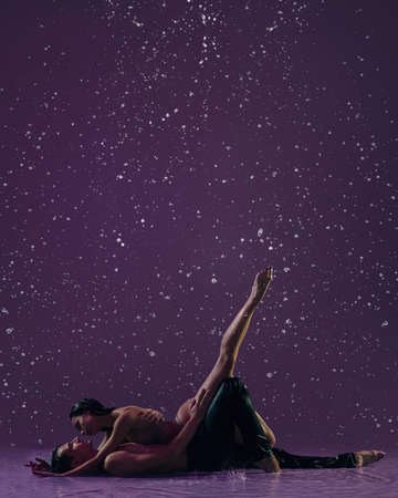 Two young ballet dancers, man and woman dancing in the raindrops over purple background. Love, art, inspiration concept.の写真素材