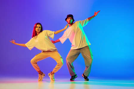 Two young people, guy and girl in casual clothes dancing contemporary dance, hip-hop over blue background in neon light.の写真素材