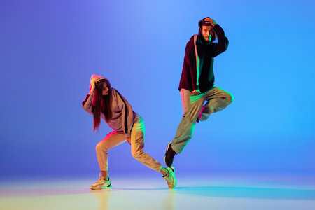 Two young people, man and woman dancing brakedance, hip-hop over blue background in neon light.の写真素材