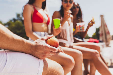Group of young people, men and women resting on the beach, drinking cool drinks, having fun, sunbathingの写真素材