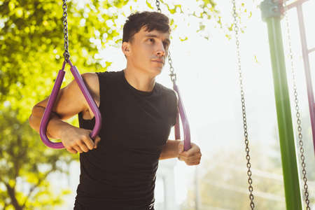 One young handsome caucasian man in sportswear doing crossfit at sports ground on bright summer day.