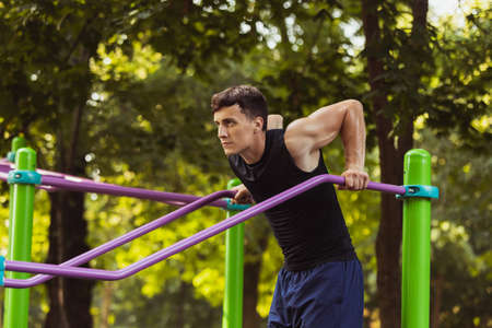 One young handsome caucasian man in sportswear doing crossfit at sports ground on bright summer day.