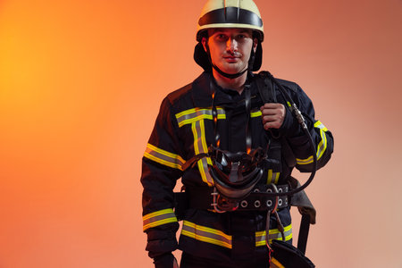 One male firefighter dressed in uniform posing over orange background in neon lights.