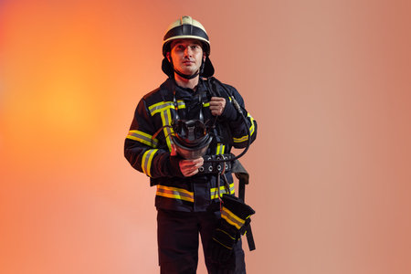 One male firefighter dressed in uniform posing over orange background in neon lights.の写真素材