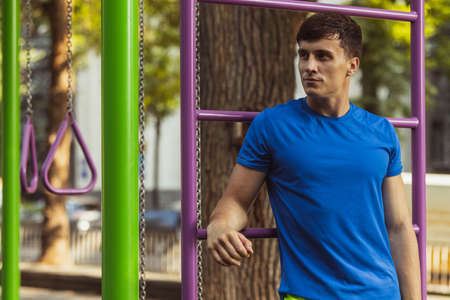 One young handsome caucasian man resting after training on sports ground outdoors on bright summer...