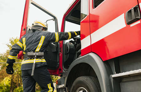 One young male firefighter dressed in uniform with protective helmet climbing into fire truck.