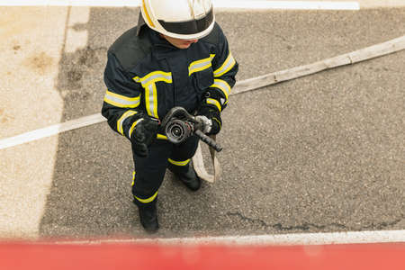 One young male firefighter dressed in uniform with water hose ready for deploymentの写真素材