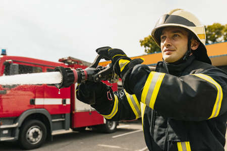 One young male firefighter on duty dressed in uniform with water hose extinguishing fireの写真素材
