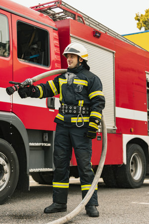 One young male firefighter dressed in uniform with water hose at fire truck ready for deploymentの写真素材
