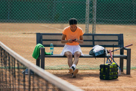 One young sportswoman, professional tennis player with phone on tennis court in bright summer day.の写真素材