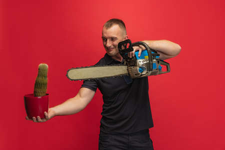 One young caucasian man with cactus and electric saw posing over red background.