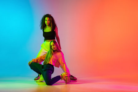 Two stylish modern girls dancing hip-hop on gradient blue orange background in neonの写真素材