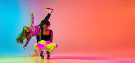 Emotive dance. Two beautiful stylish hip-hop girls dancing on colorful gradient background in neon lightsの写真素材