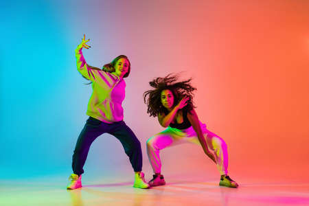 Two beautiful stylish hip-hop dancers on colorful gradient background in neon lightsの写真素材